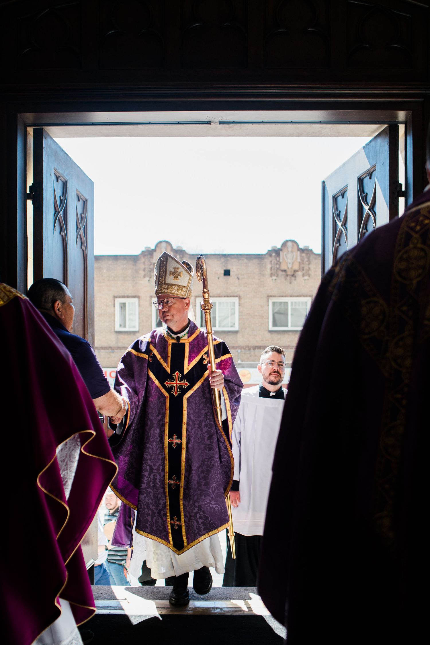 A line of people in purple and black graduation robes walking through a doorway.