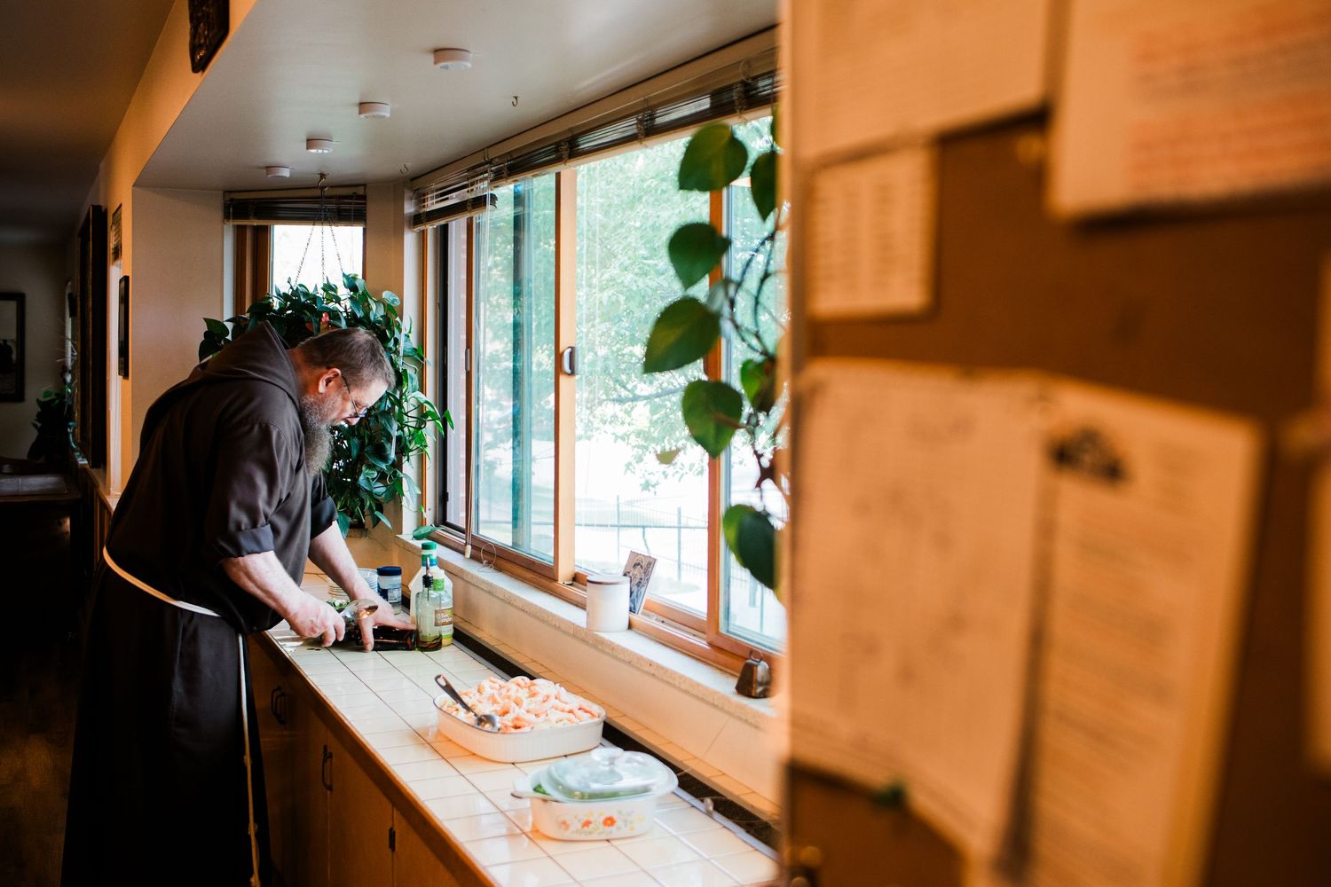 Chef preparing food at a wooden counter beside large windows in a cozy restaurant kitchen.
