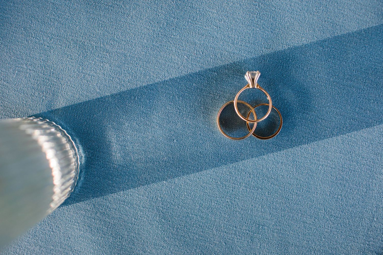 Three gold wedding rings with diamond engagement ring displayed on blue velvet fabric.