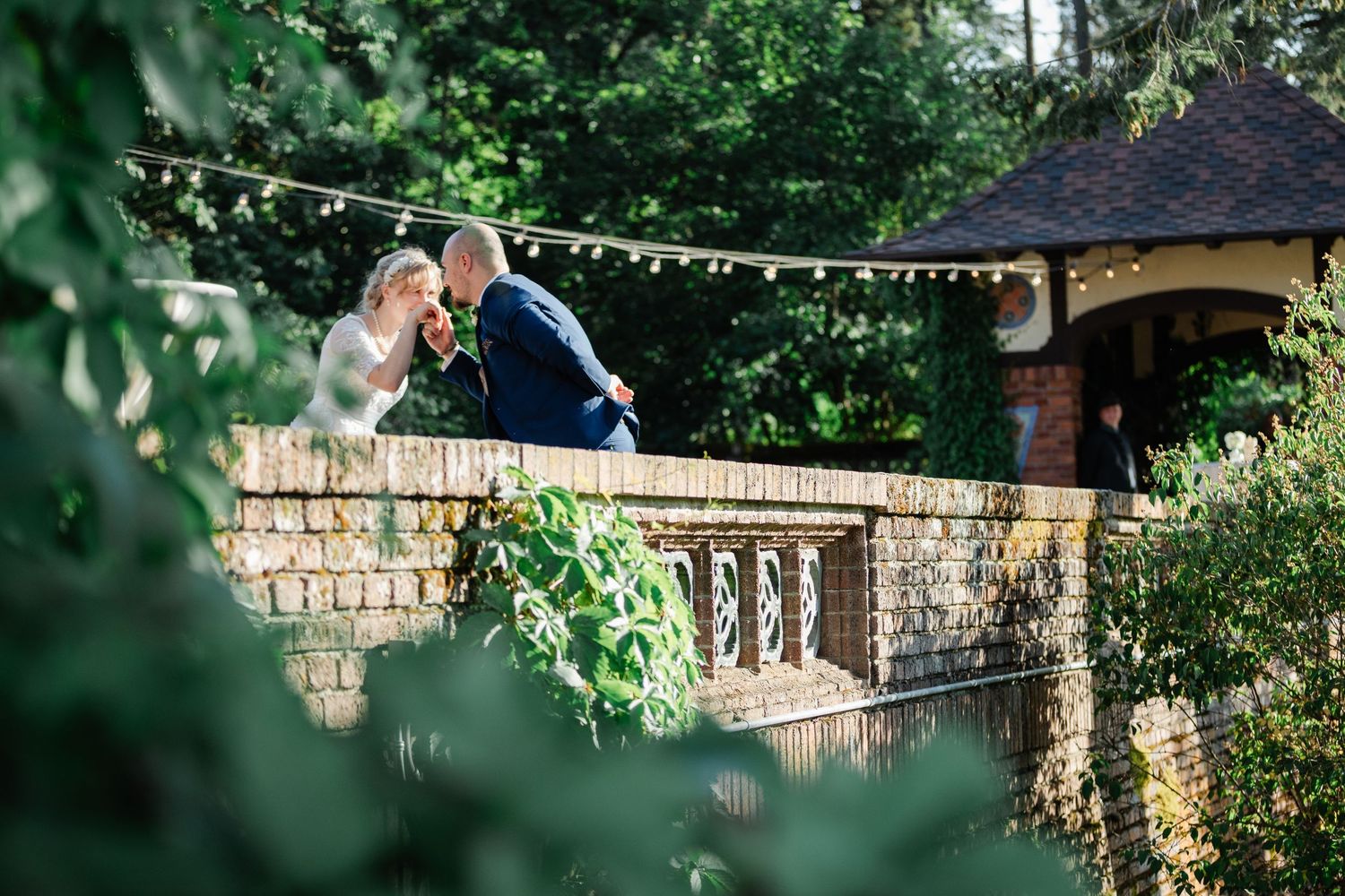 Bride and groom share a romantic moment on a stone bridge surrounded by lush greenery.