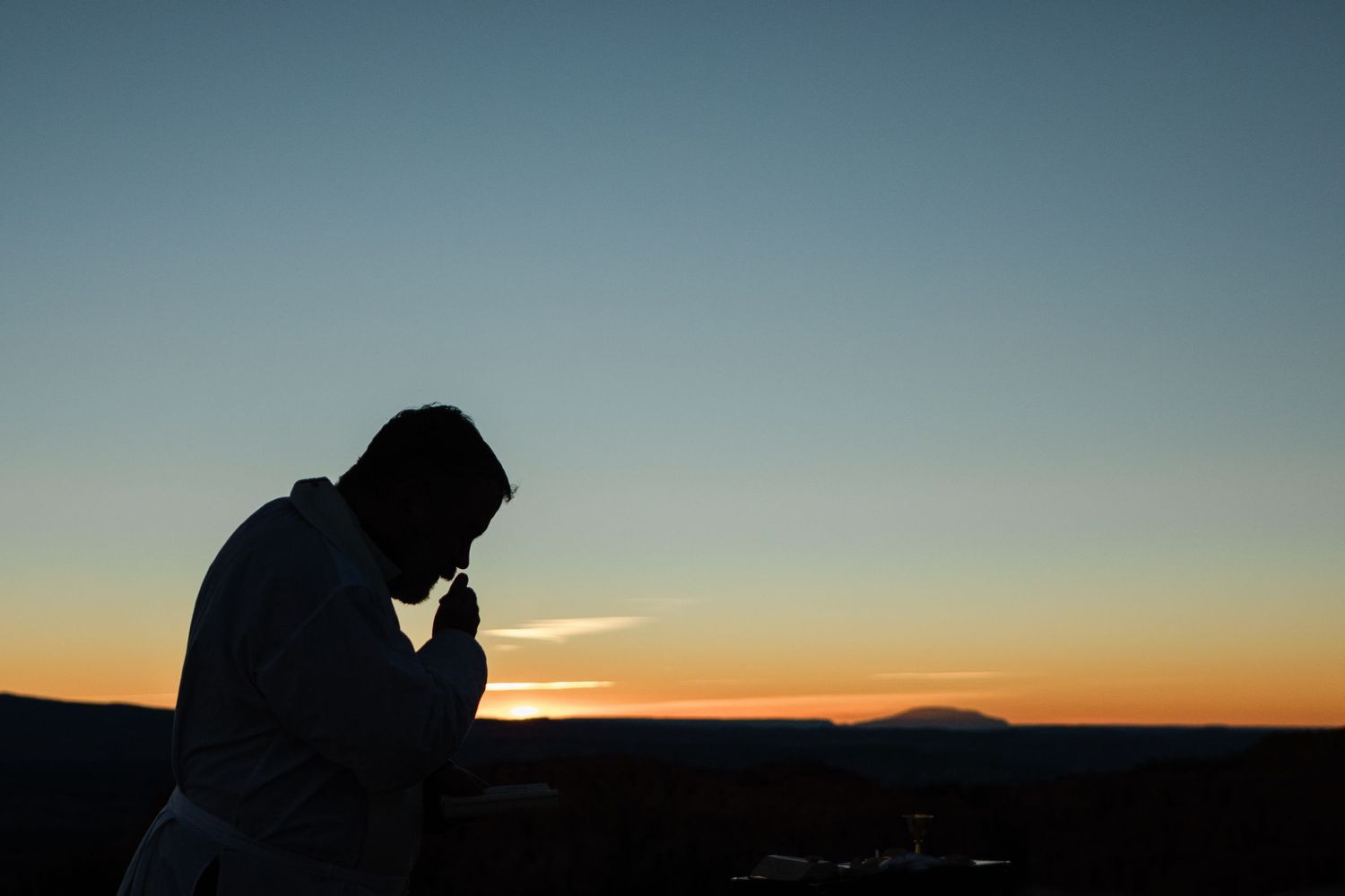 Silhouettes of people watching a vibrant orange and blue sunset over mountain peaks in the distance.