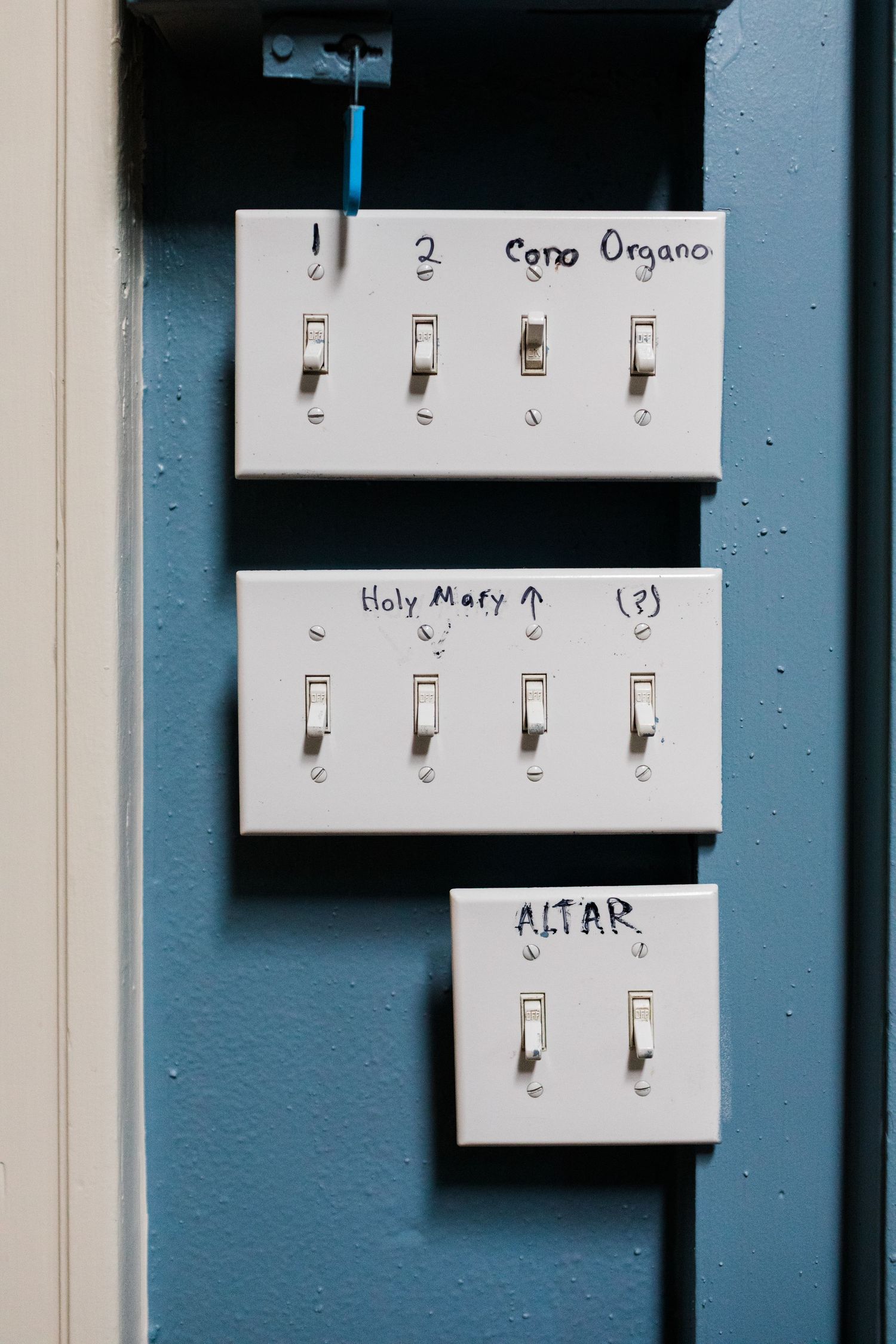 White key hooks mounted on blue wall with handwritten labels above them.