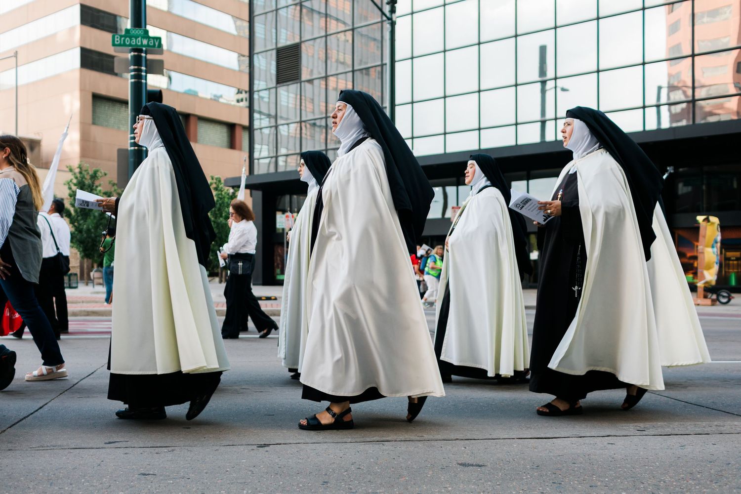 Group of Catholic nuns in traditional black and white habits walking across a city street crosswalk.
