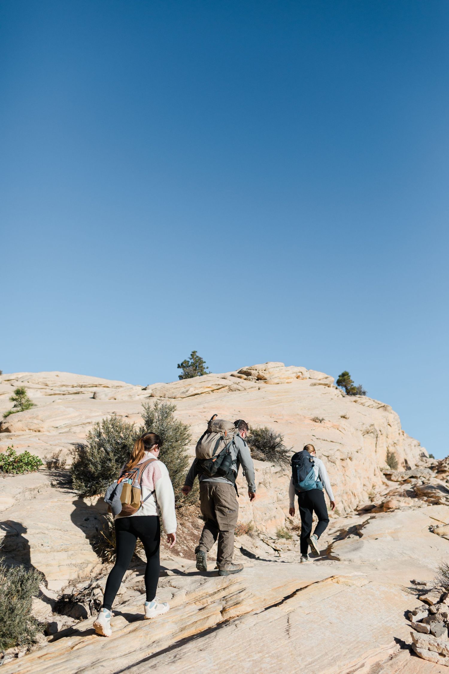 A group of hikers climb up a steep sandstone rock formation under clear blue skies.