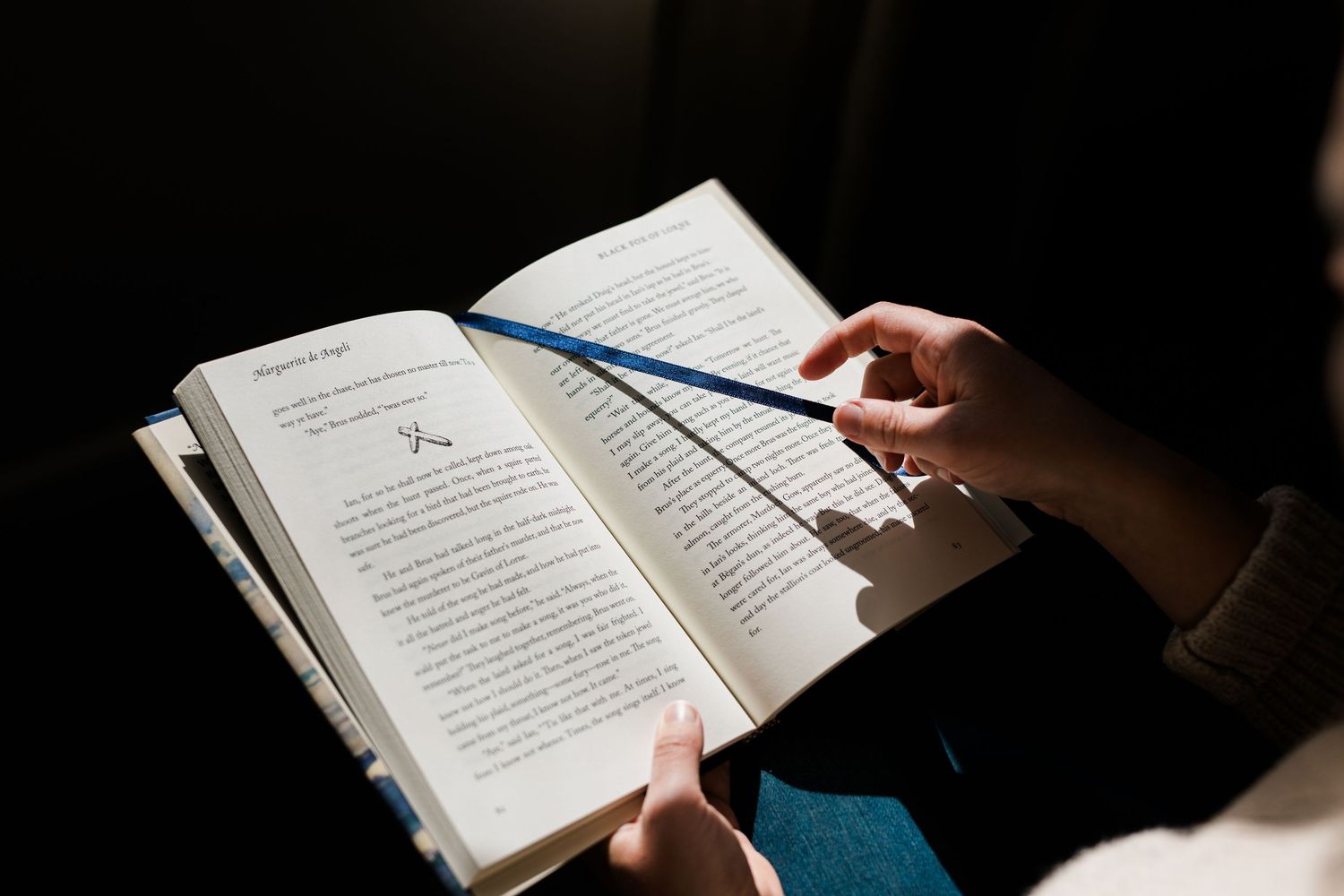 A series of hands holding open books in dark lighting conditions showing pages of text.