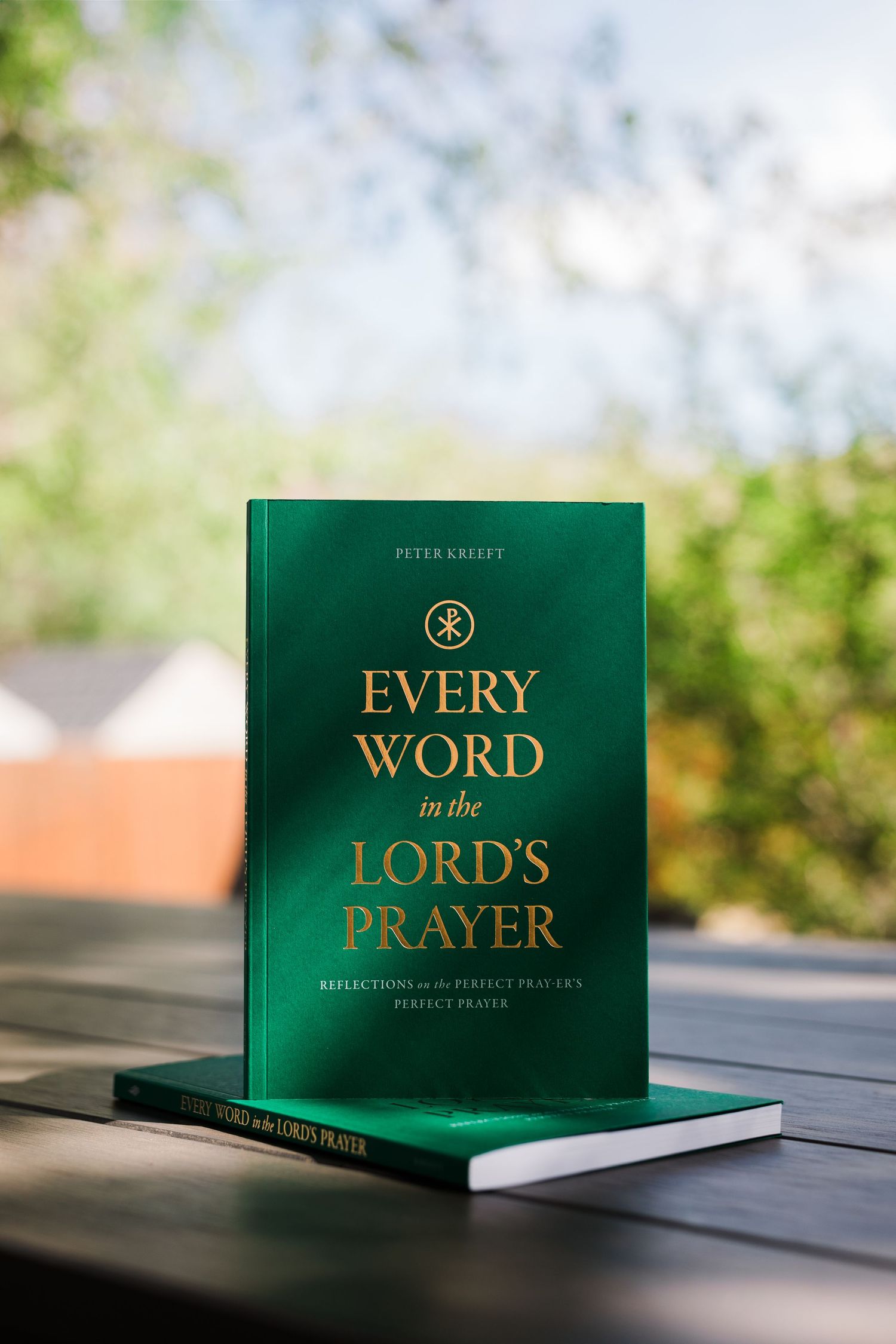 Green hardcover 'Every Word in the Lord's Prayer' by Peter Kreeft standing upright on outdoor table.