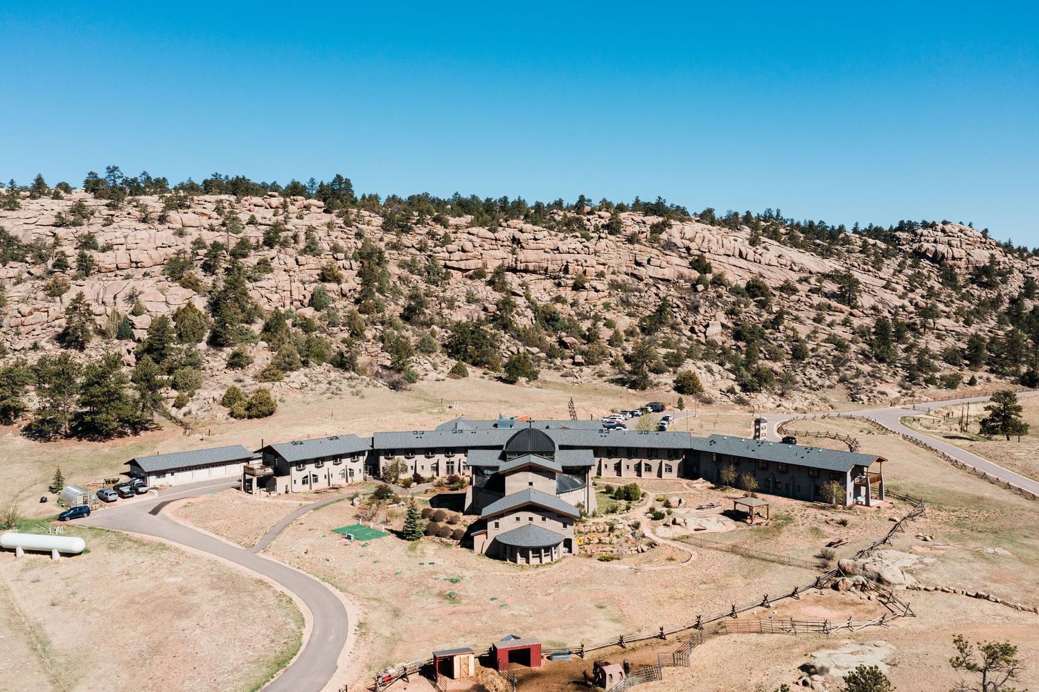 Aerial view of a rustic ranch lodge nestled among rocky hills and pine trees in a dry Colorado landscape.