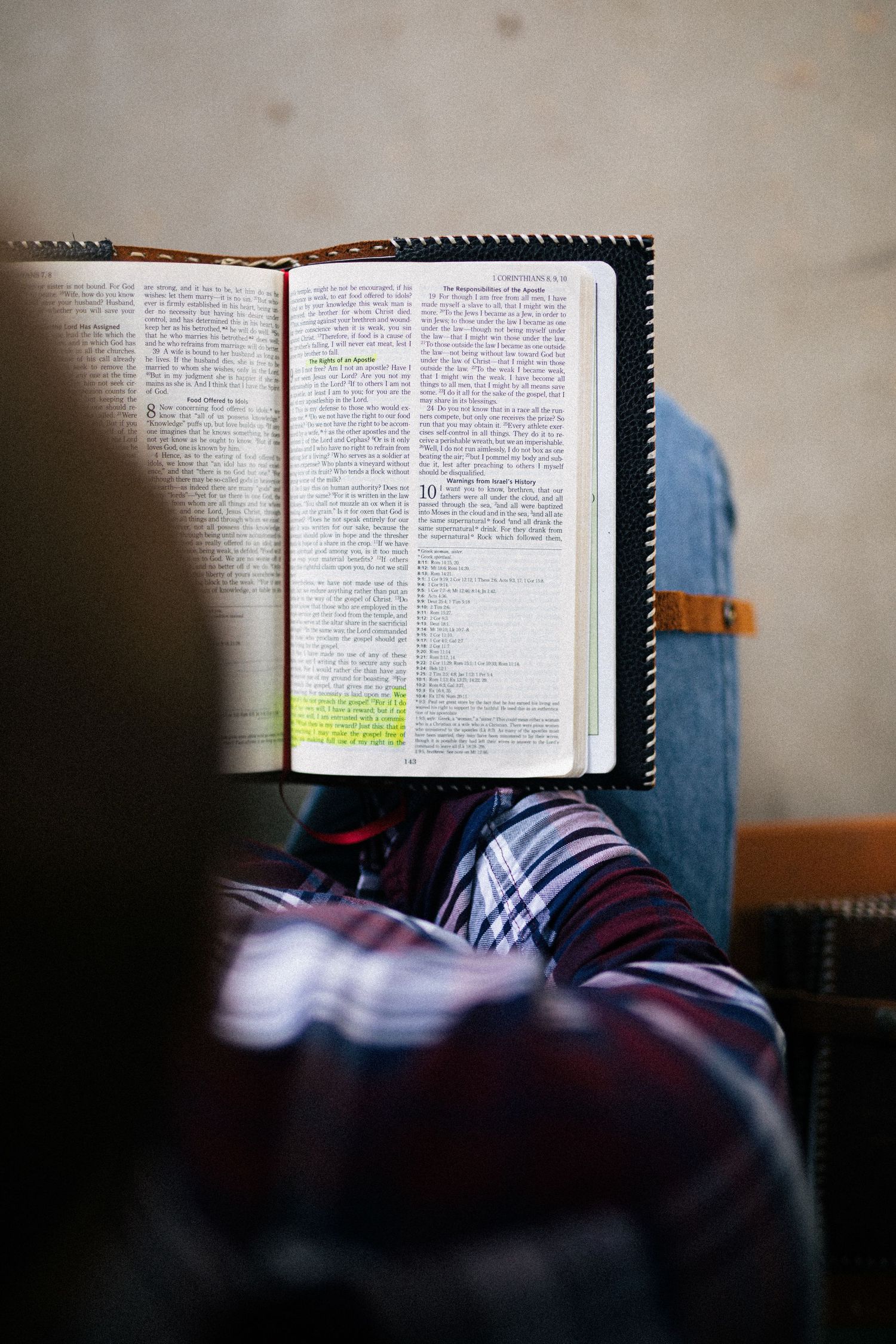 Open Bible with highlighted text being read by someone wearing plaid fabric in a study setting.