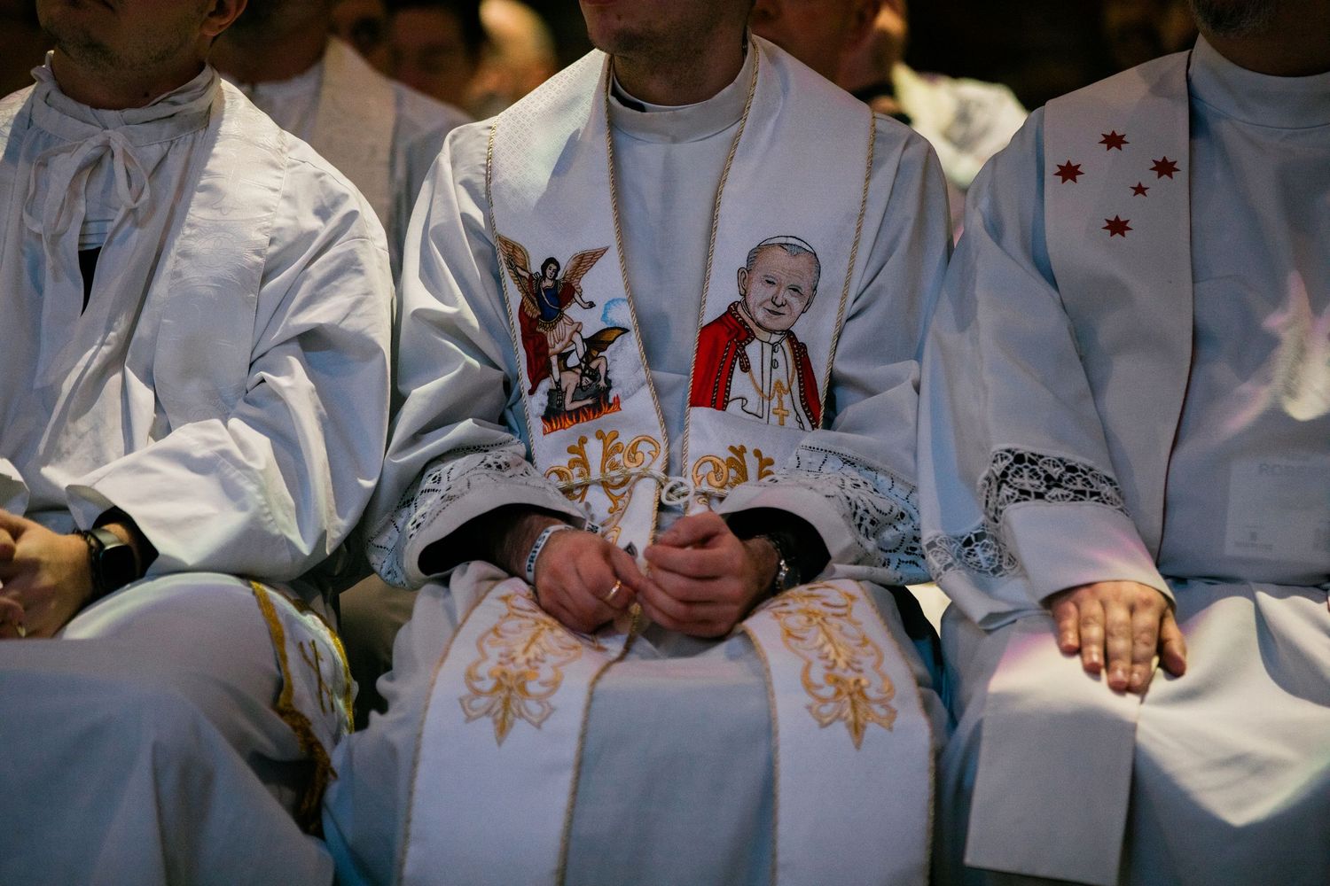 Row of white-robed figures seated with hands clasped.