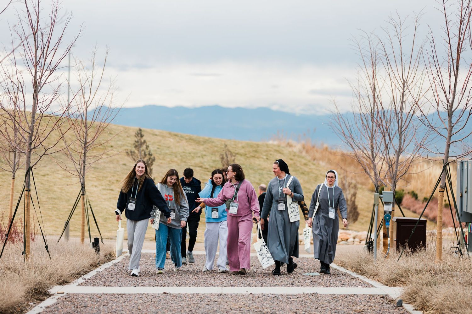 A group of people stand together on a path against a backdrop of bare trees and mountains in winter.