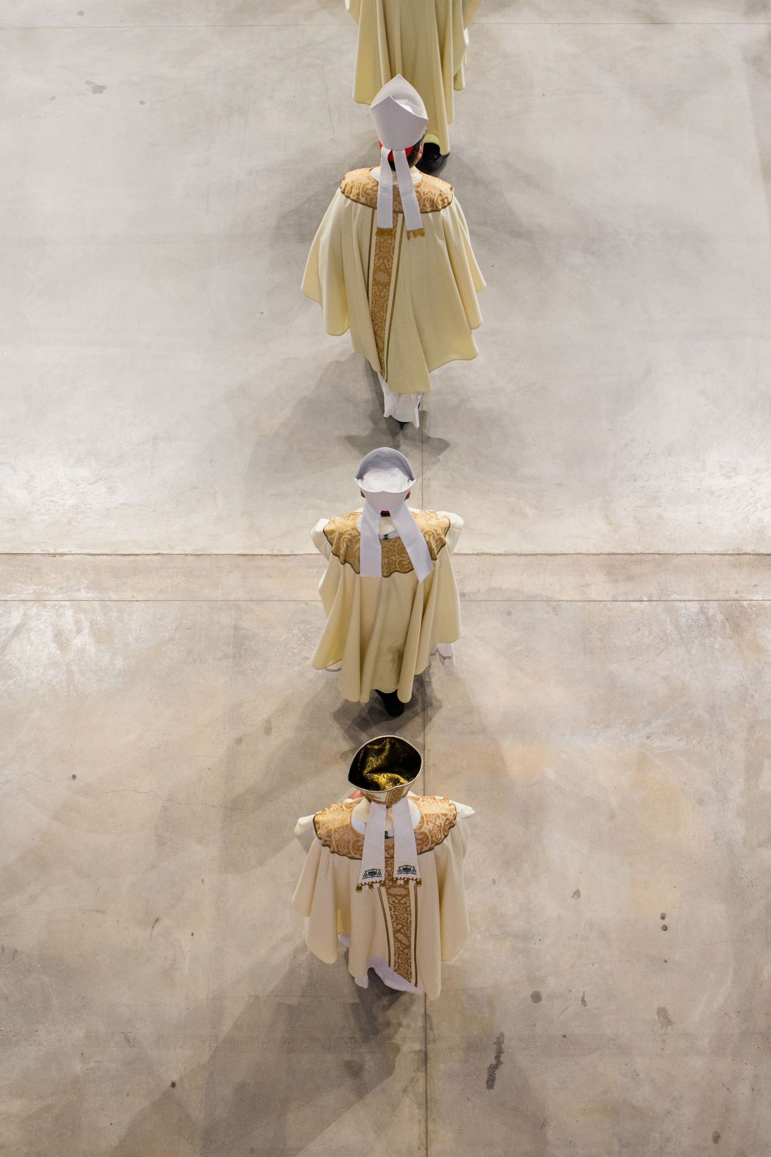 A line of graduates in yellow robes and caps walk across a concrete floor during a commencement ceremony.
