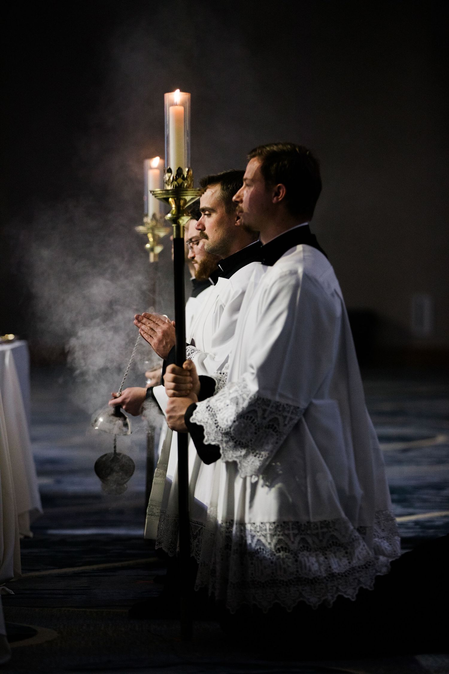 A sequence of dramatic candlelit photos showing figures in white robes holding candles against a dark background.