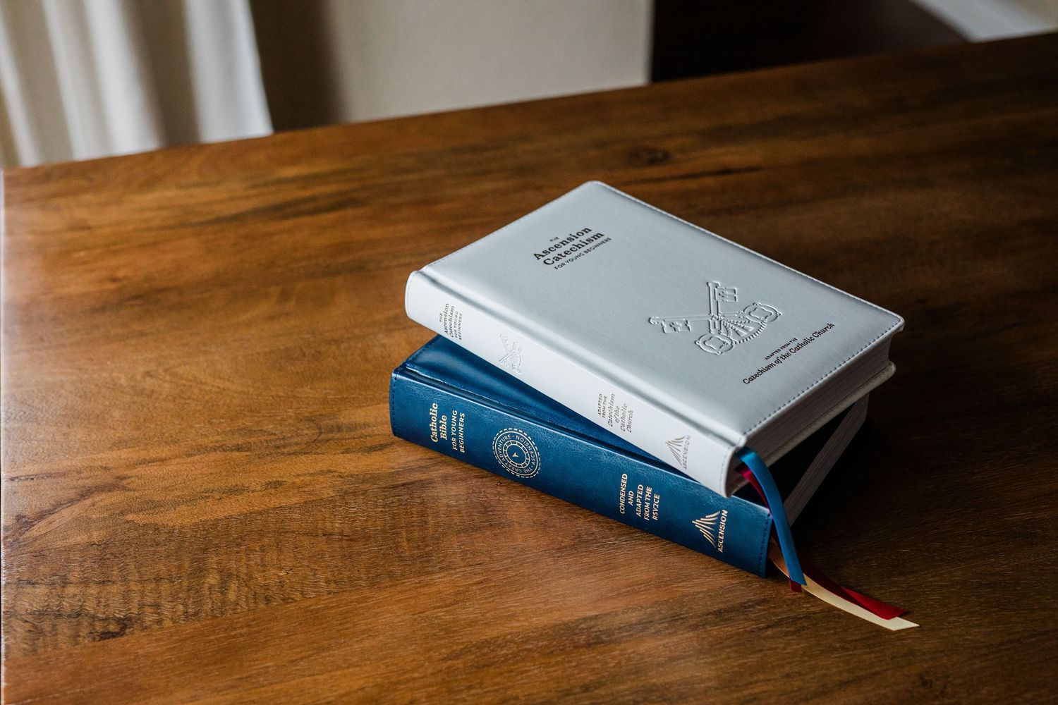White and blue hardcover books stacked on a wooden table with ribbon bookmark.
