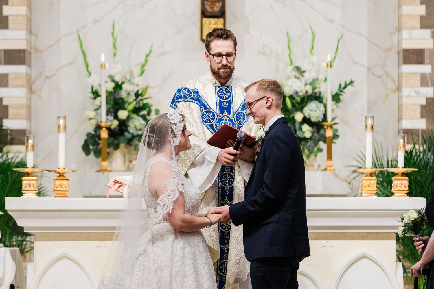 Bride and groom exchange vows at elegant church altar with officiant holding ceremony book.