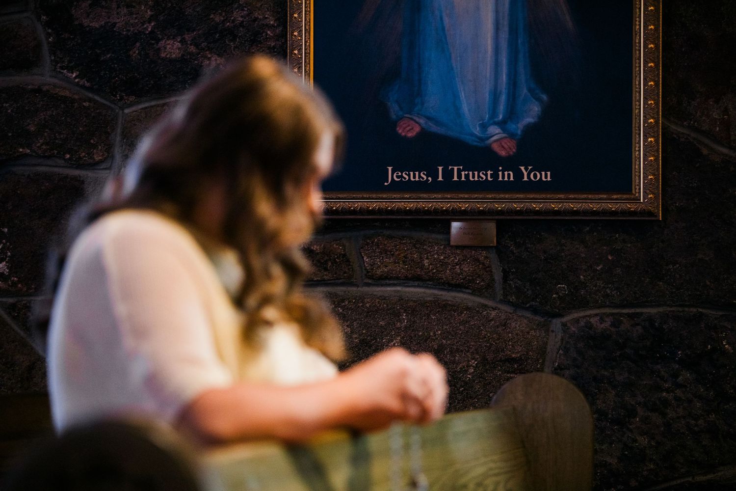 Woman praying before a Divine Mercy painting with Jesus, I Trust in You inscription in a church.