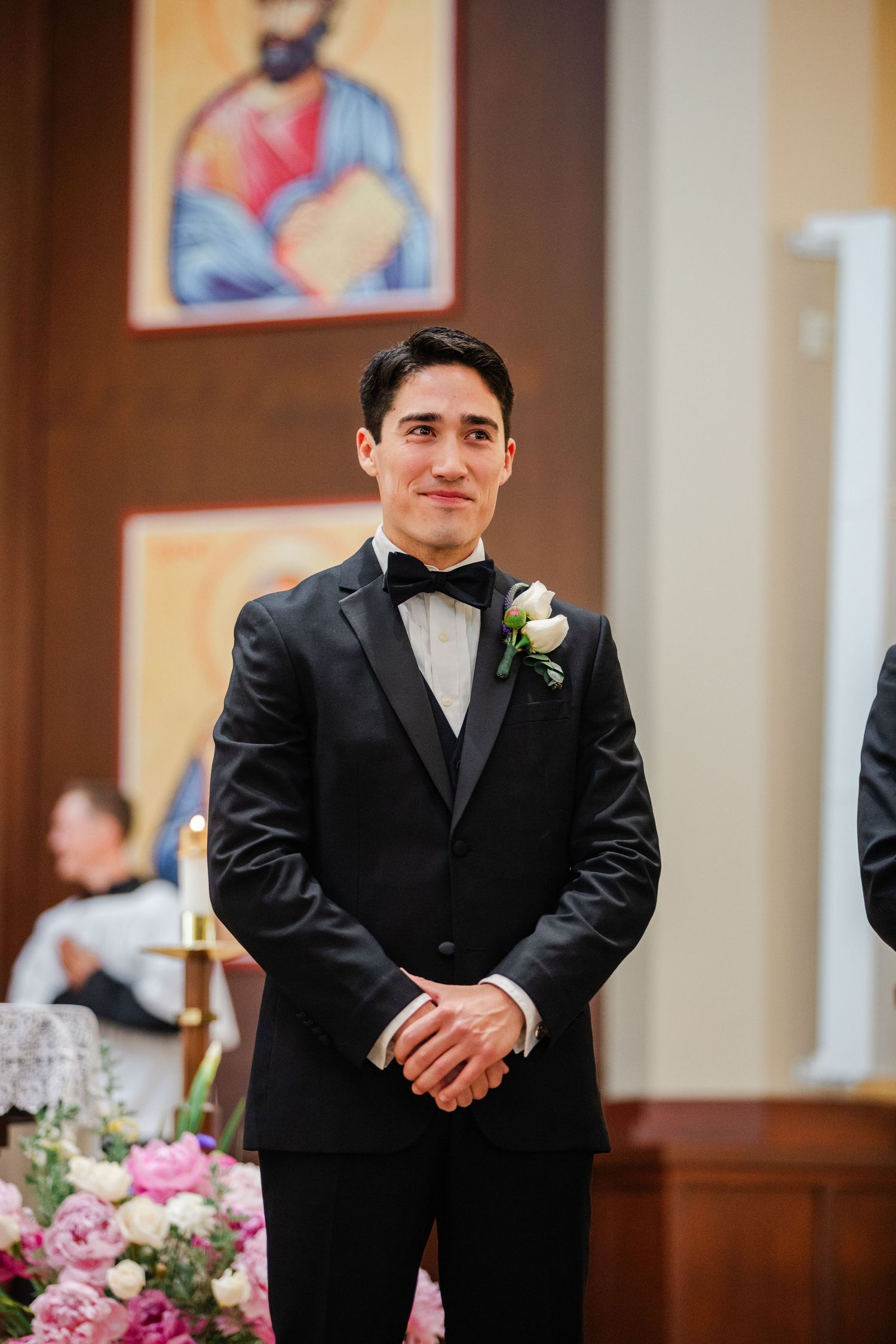 Groomsmen in black tuxedos stand at the altar during an elegant indoor wedding ceremony.