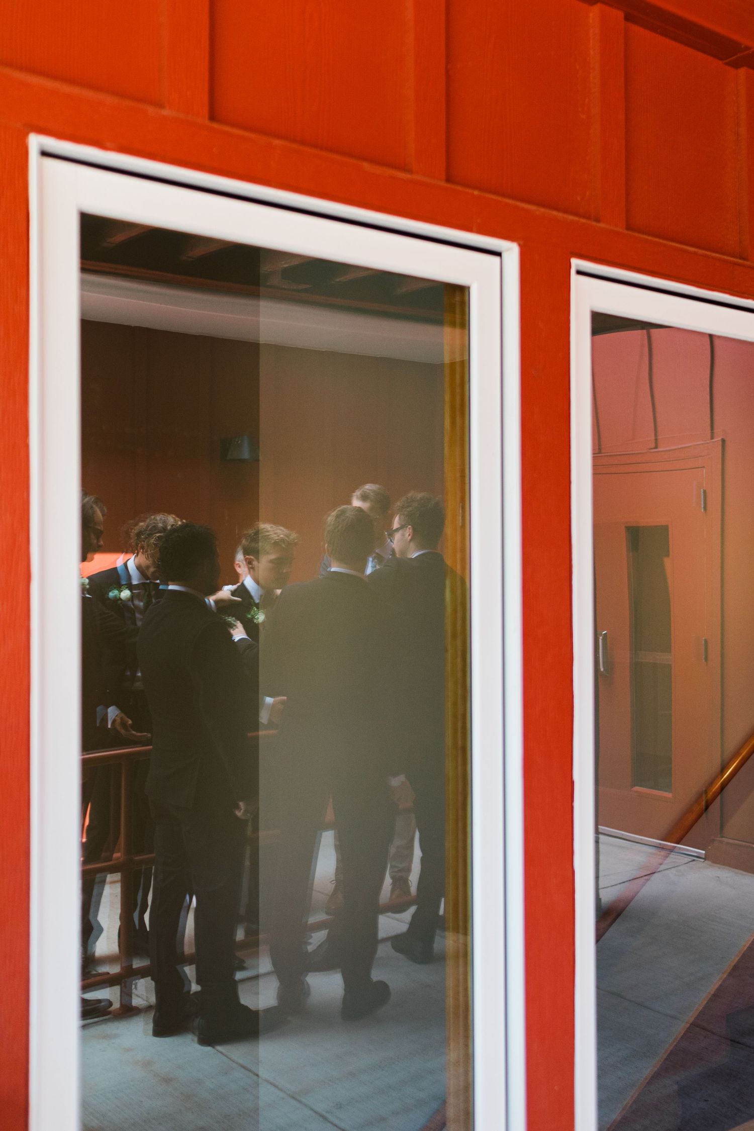 A group of people seen through a glass door with a bright red exterior wall.