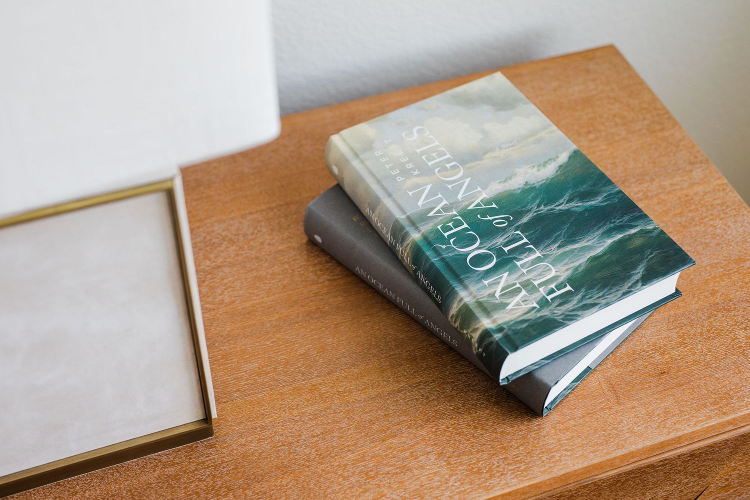 Two hardcover books stacked on a wooden side table next to a framed artwork.