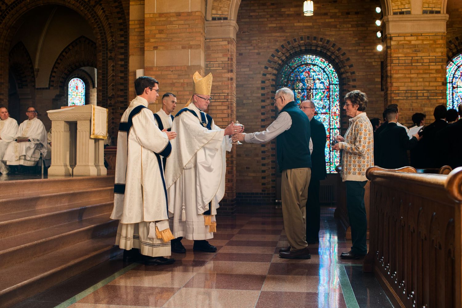 Catholic bishop in ceremonial vestments greeting parishioners during a church service inside a brick cathedral.