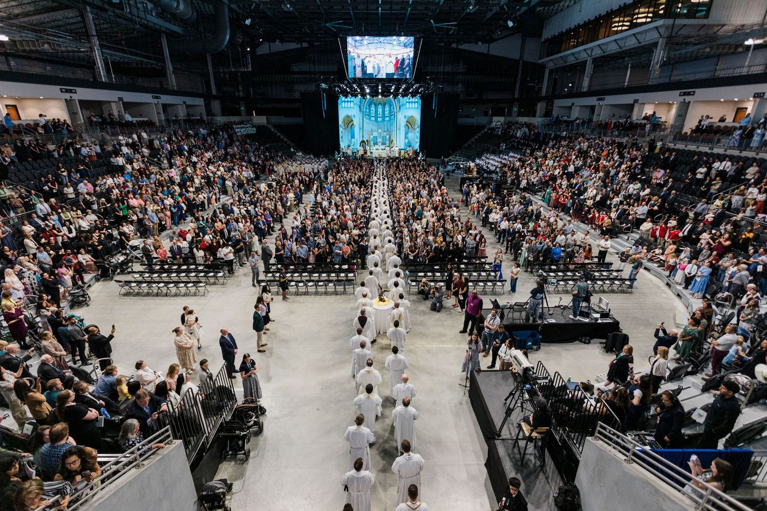 Large crowd gathered in an indoor arena during a religious ceremony or mass event.