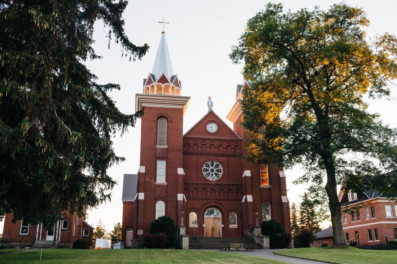 A series of red brick church buildings with steeples photographed from different angles during sunset in rural scenery.