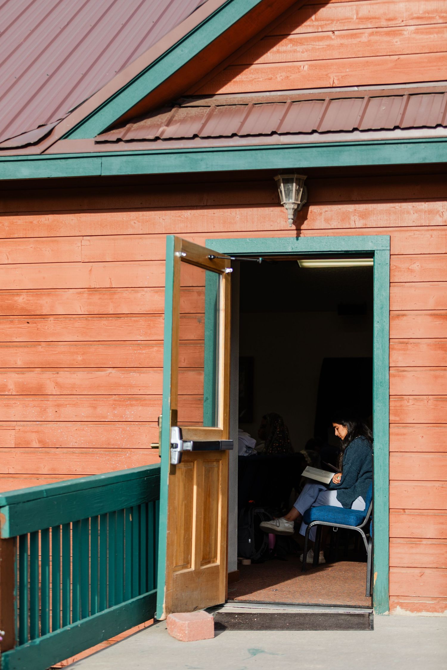 Orange and teal colored cabin with a deck and multiple windows in a rustic setting.