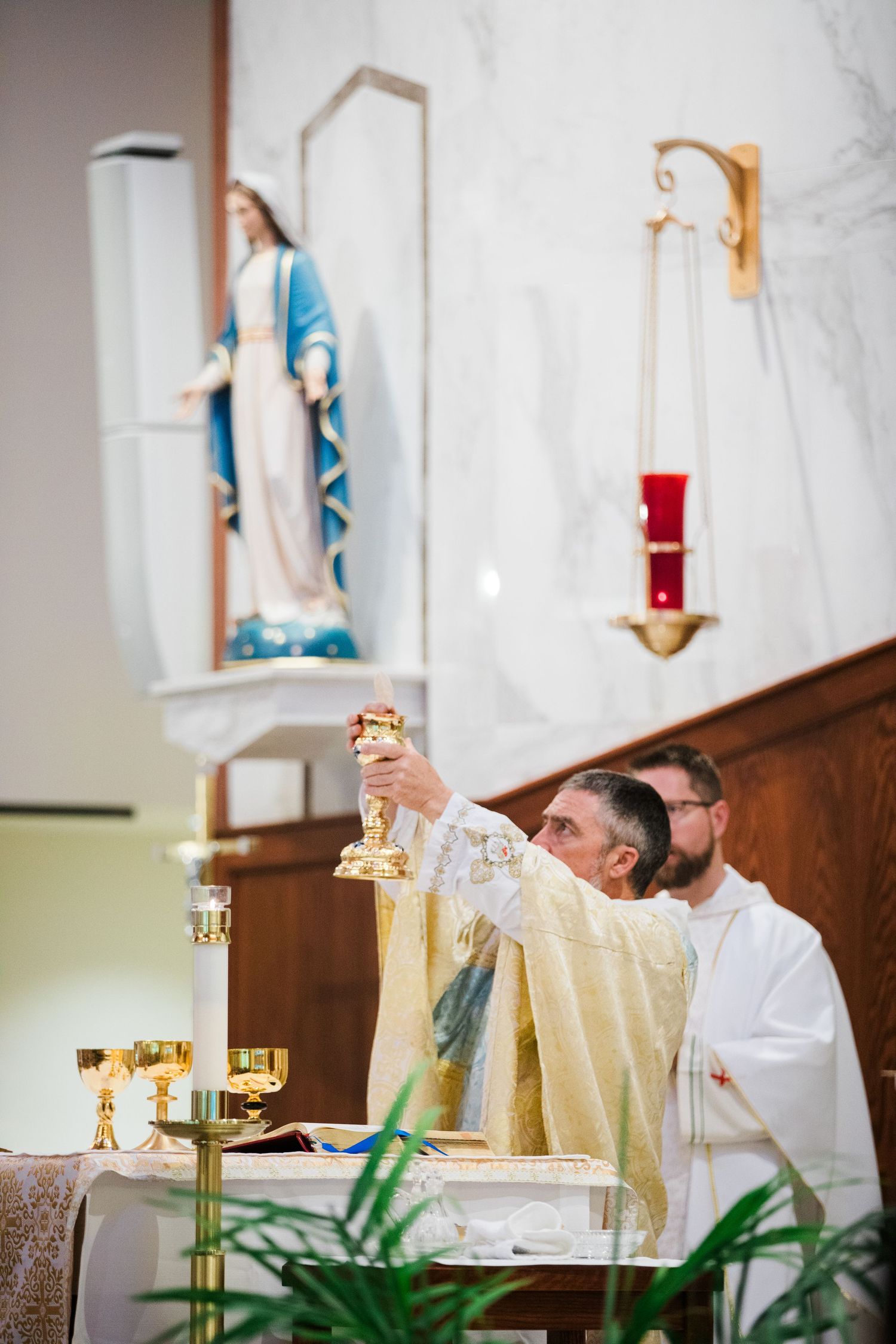 Priest performing religious ceremony at church altar with golden chalice and white linens.