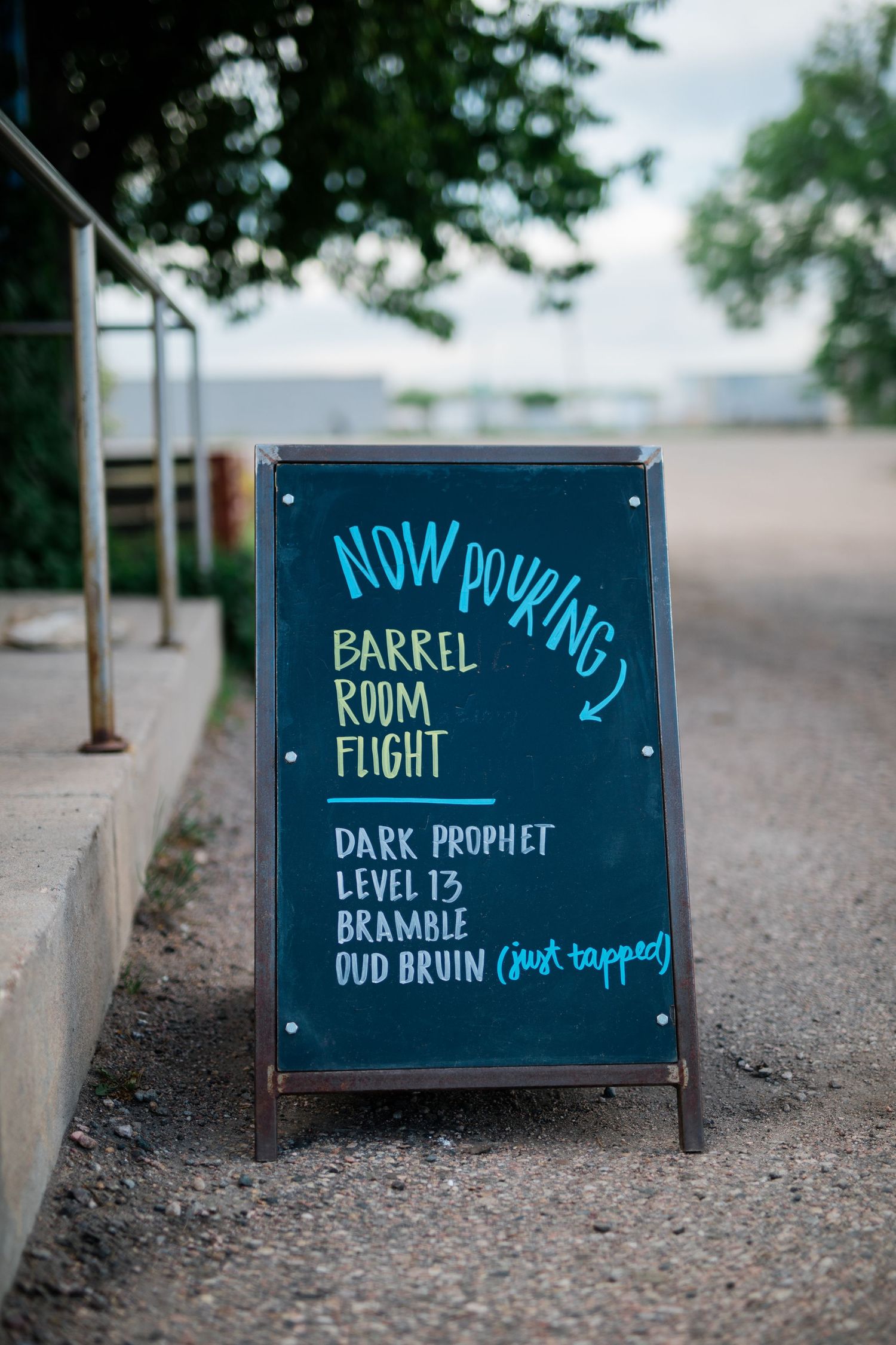 Row of chalkboard signs displaying craft beer names and types on a gravel path.