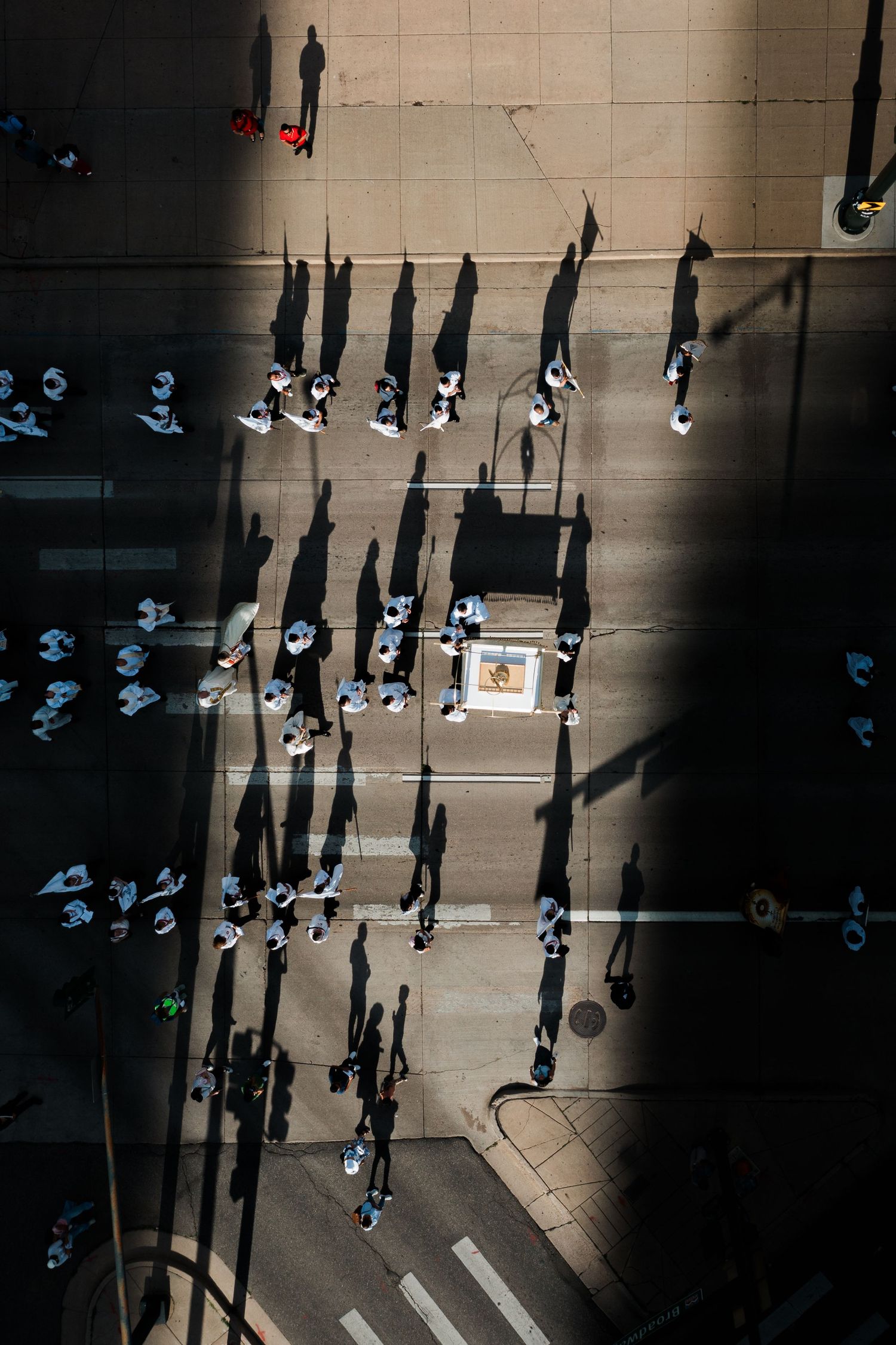 Aerial view of people casting long shadows on a city sidewalk, creating a dramatic geometric pattern in sunlight.