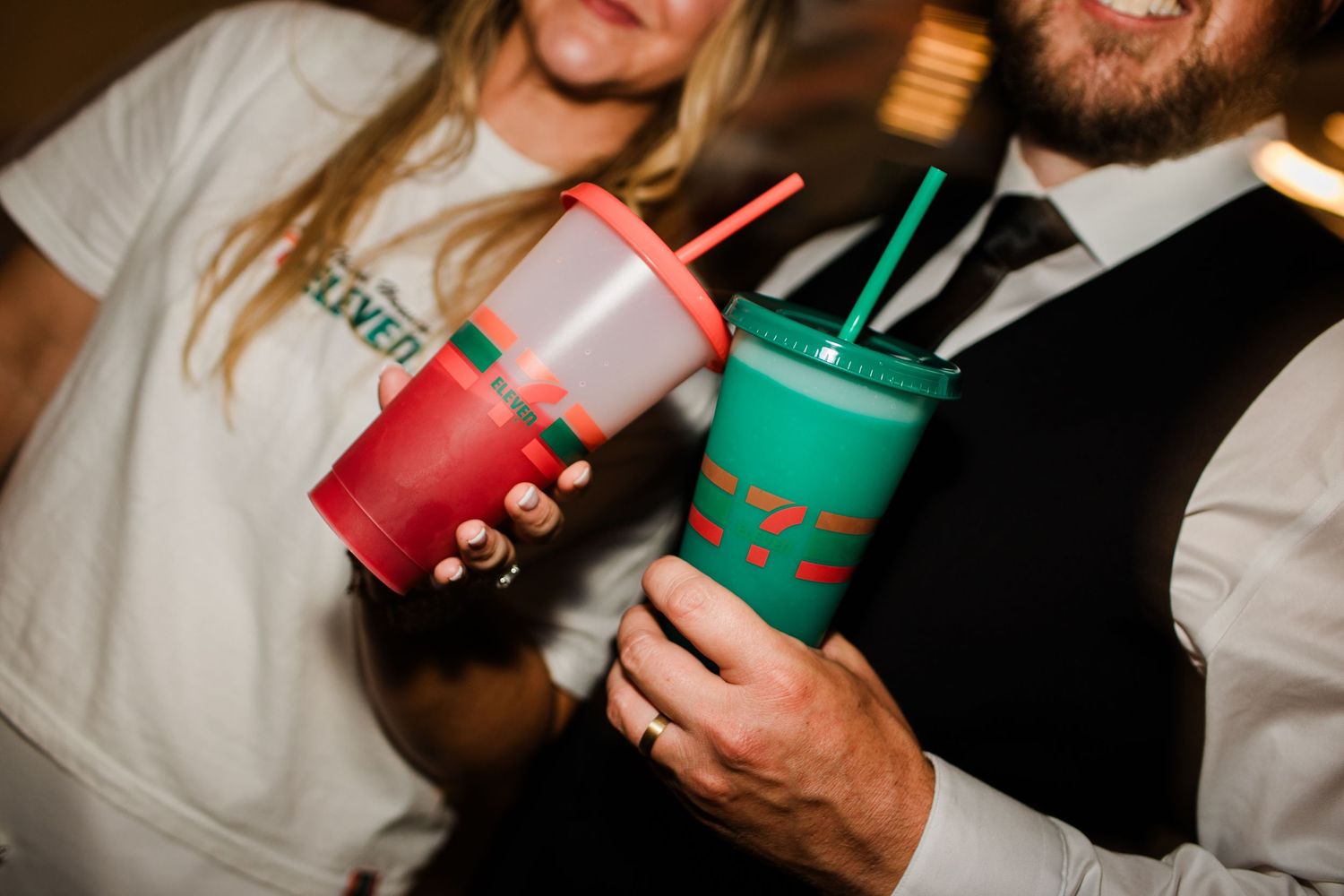 Couple holds colorful 7-Eleven cups at wedding reception in casual celebration attire.