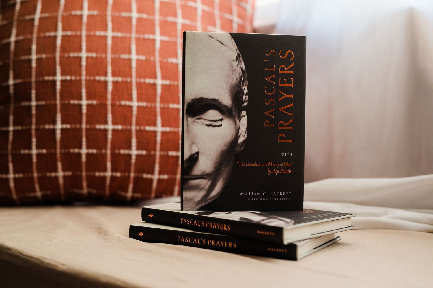 Stack of Pascal's Prayers books by William J. Brickey displayed on a wooden surface near a cushion.