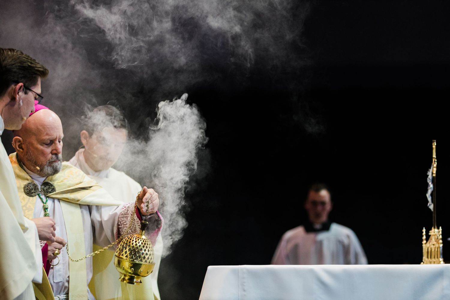 Catholic priest swings a smoking thurible of incense during a religious ceremony at the altar.