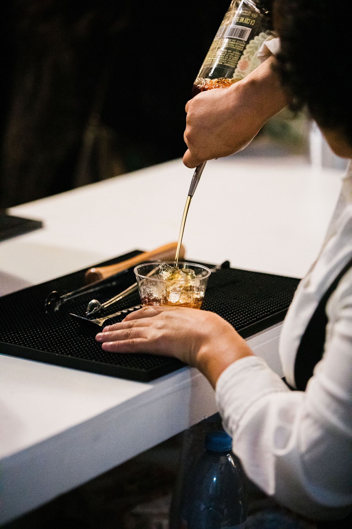 Bartender pouring drinks at a white counter with professional bar equipment.
