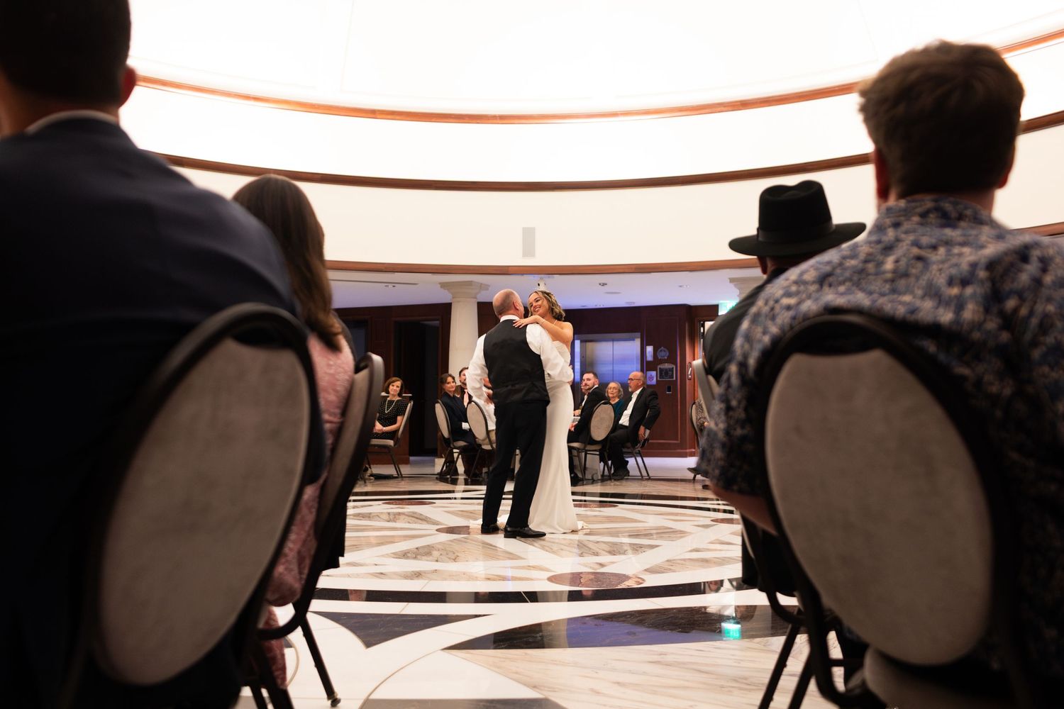 Guests seated in chairs watch a couple share their first dance at an elegant wedding reception venue.