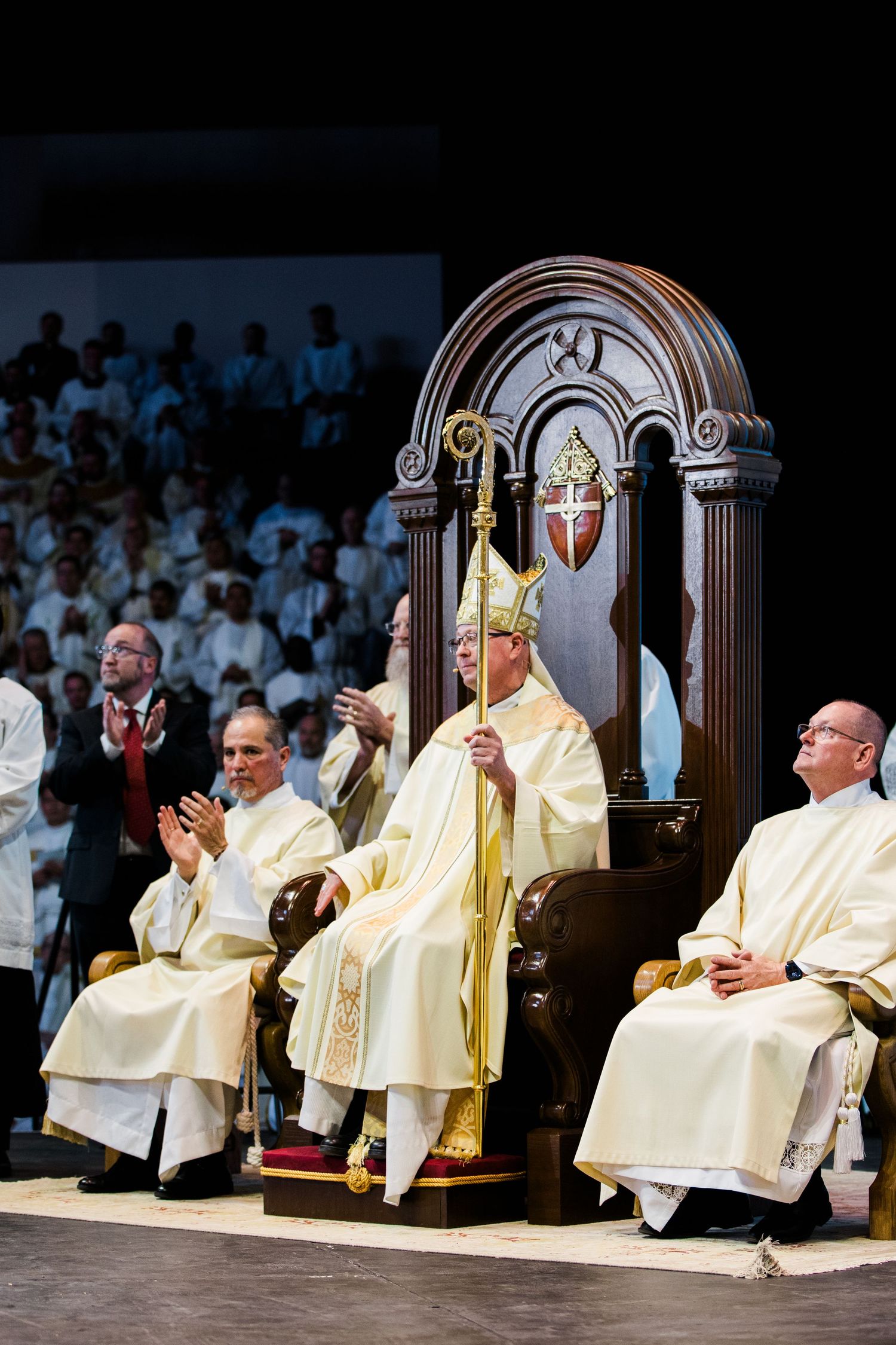 Newly ordained Catholic bishop seated on ornate wooden throne holding crosier during episcopal ordination ceremony.