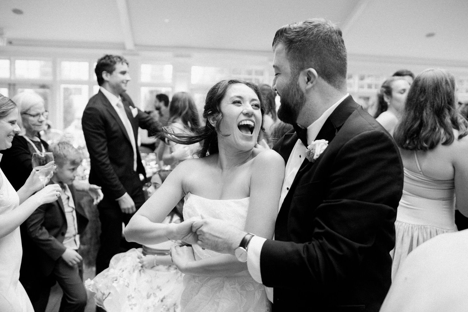 Black and white photo of a laughing bride and groom sharing a joyful dance at their wedding reception.
