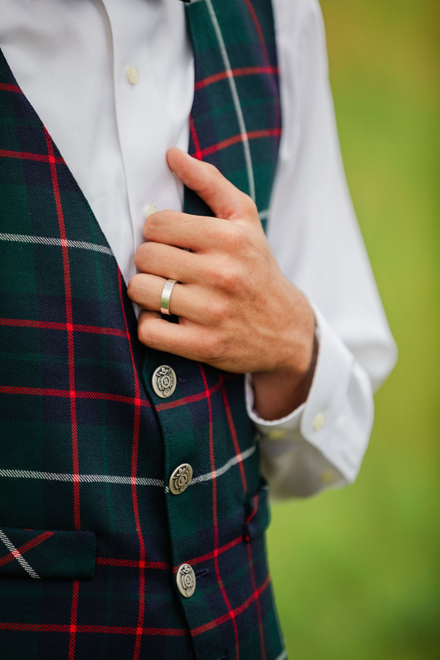 Close-up details of a plaid vest with silver buttons and a white shirt against a green background.