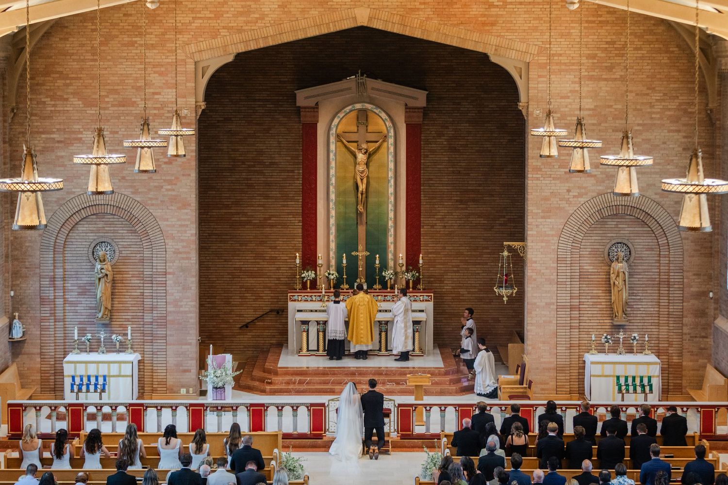 A panoramic view of a church interior with brick walls, hanging pendant lights, and a traditional altar setup.