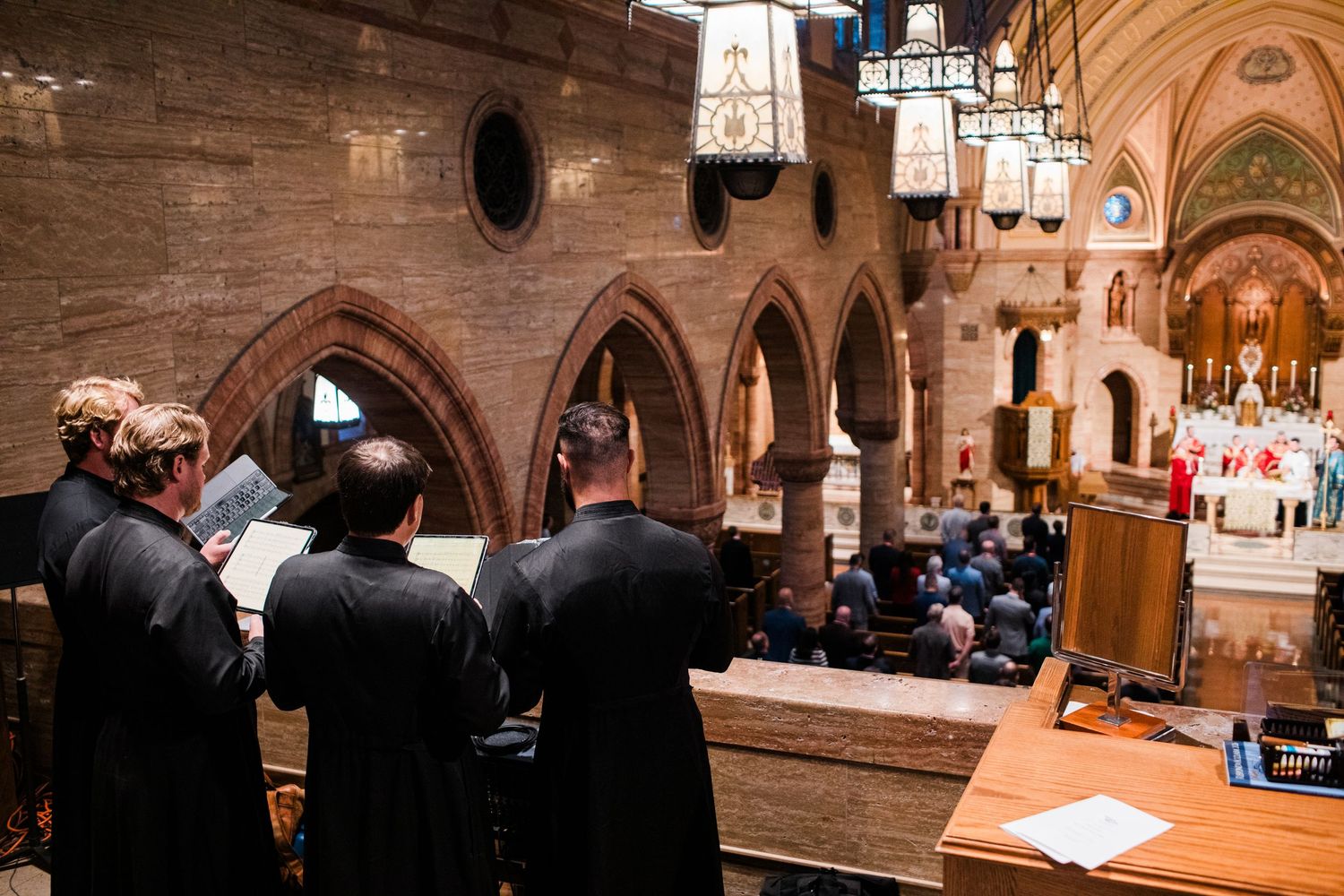Choir members in black robes performing in ornate Gothic cathedral during religious ceremony.