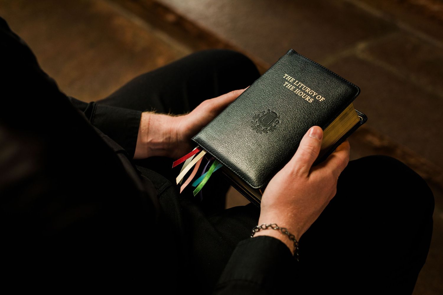 Person holding a black leather Liturgy of the Hours book with colorful ribbon bookmarks.