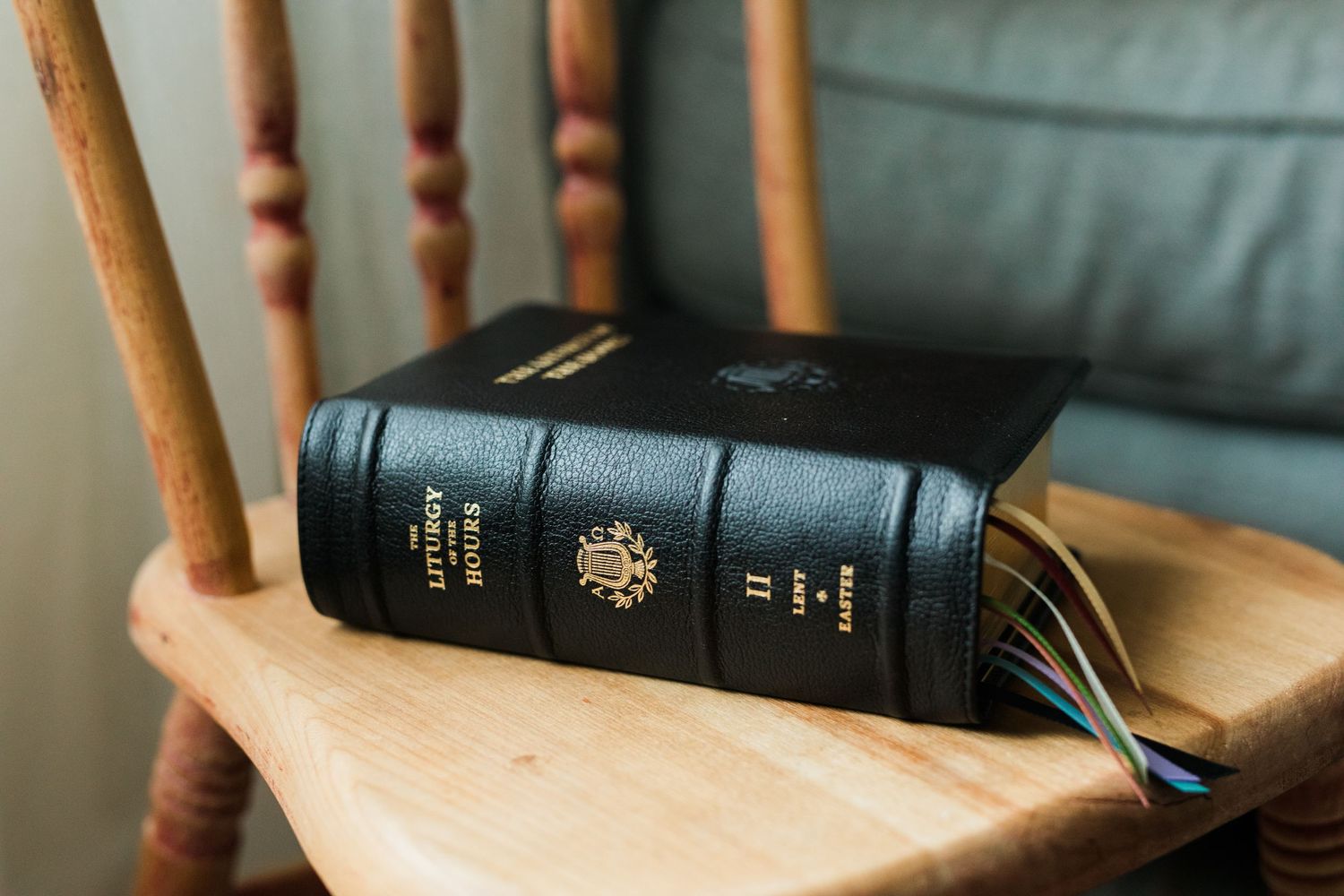 Black leather Bible with gold embossing resting on a wooden rocking chair arm.