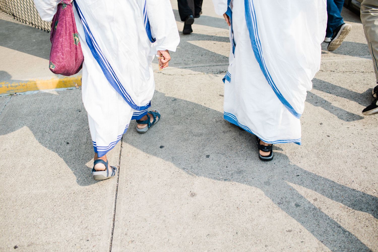 People in white robes with blue stripes walking along a sidewalk.