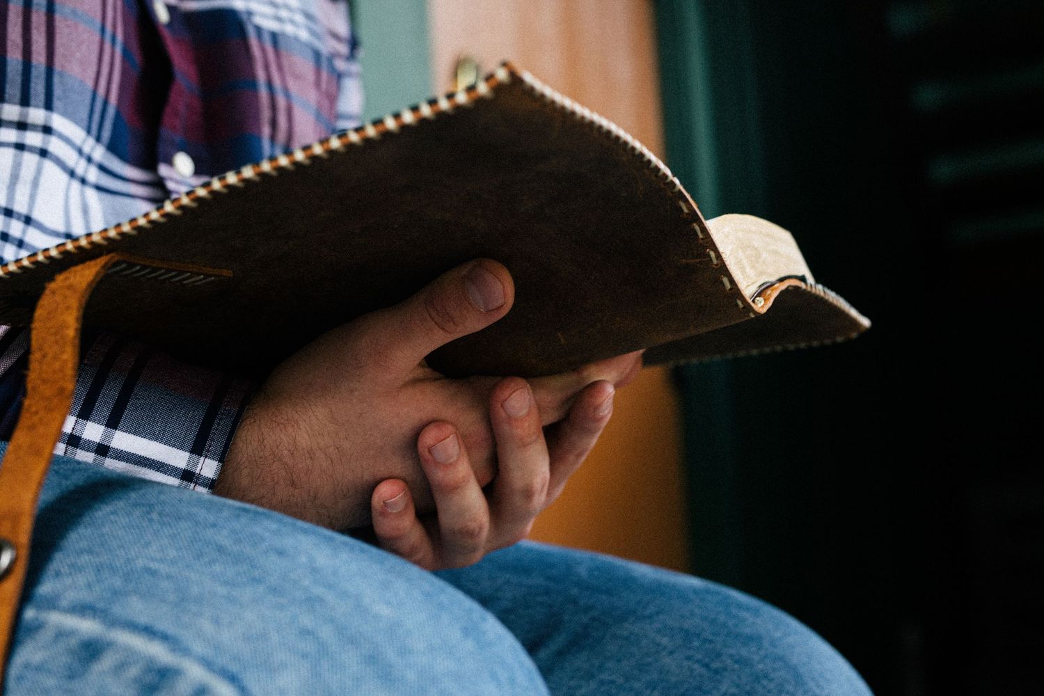 Person wearing plaid shirt checks their smartphone and tablet device in sunlit workspace.