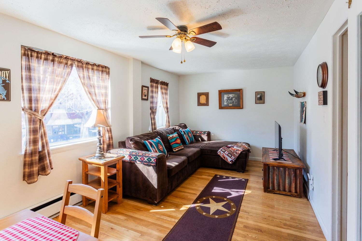 A cozy living room with a plaid sofa, wooden furniture, and a ceiling fan providing comfortable ambiance.