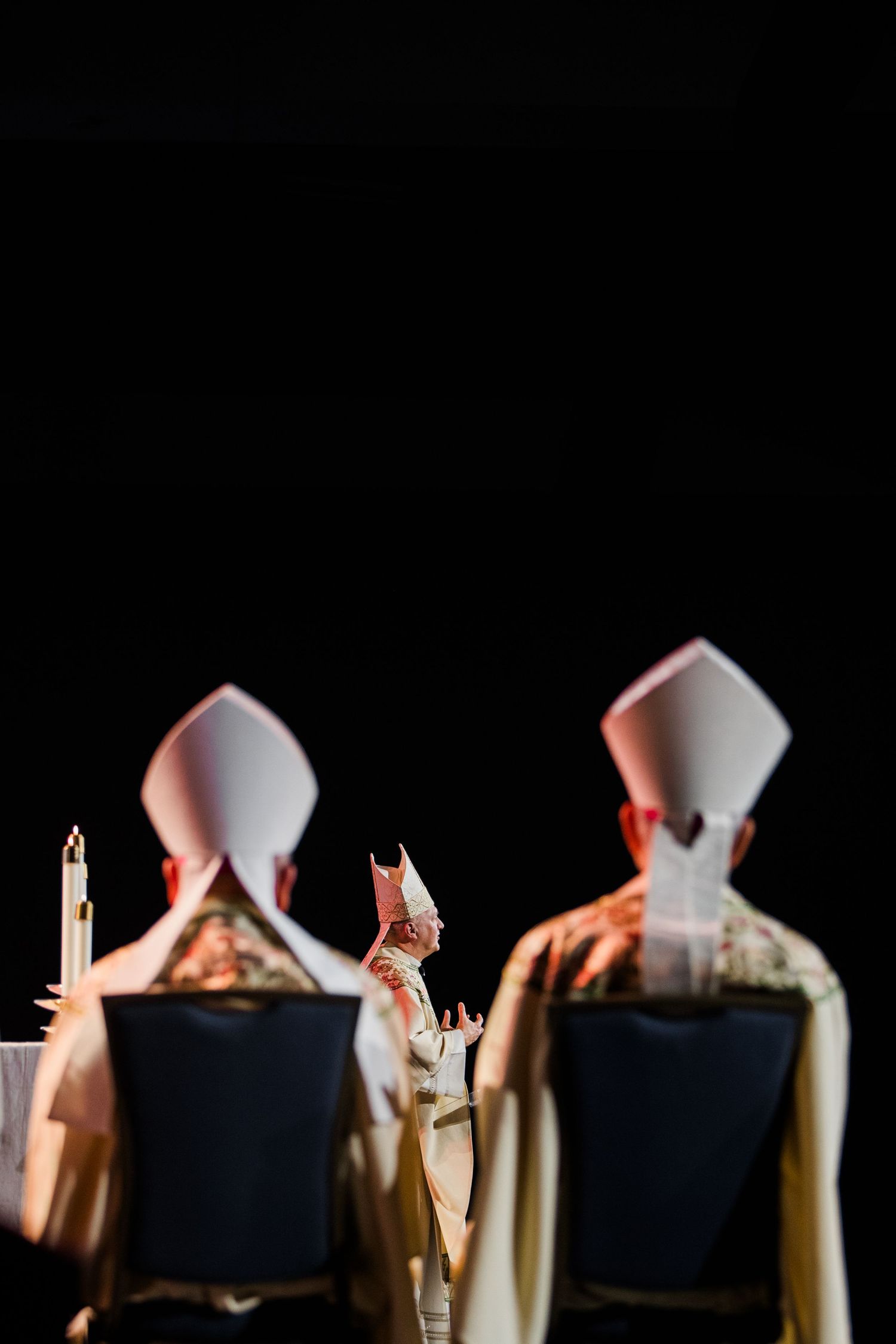 Silhouetted figures in religious vestments with candles against a dark background.