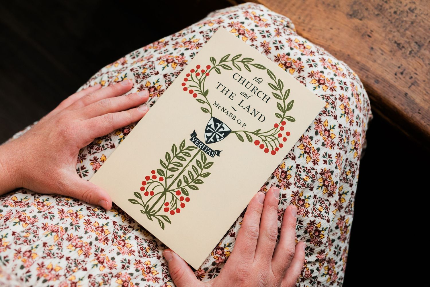 A floral patterned tablecloth with hands holding an open book with decorative green and red designs.