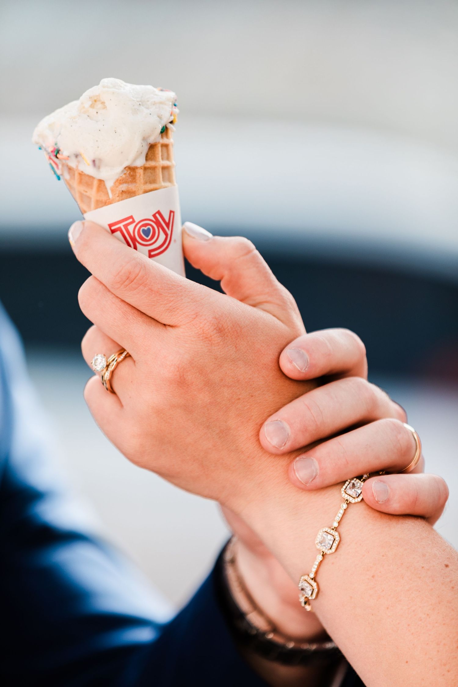Newlyweds holding a Joy ice cream cone together, showing wedding rings and bracelet.