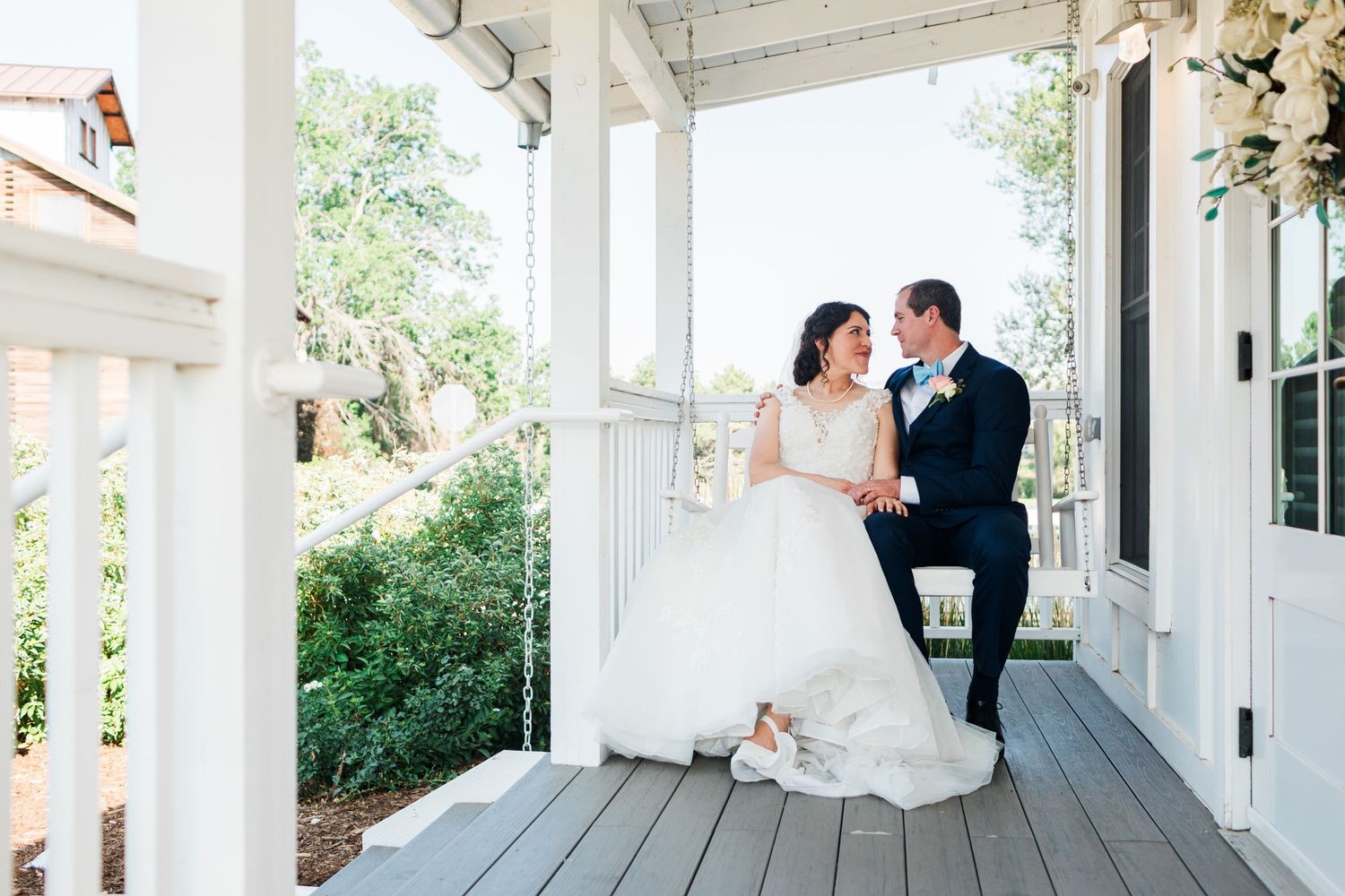 Bride and groom share a romantic moment on a white porch surrounded by lush greenery.