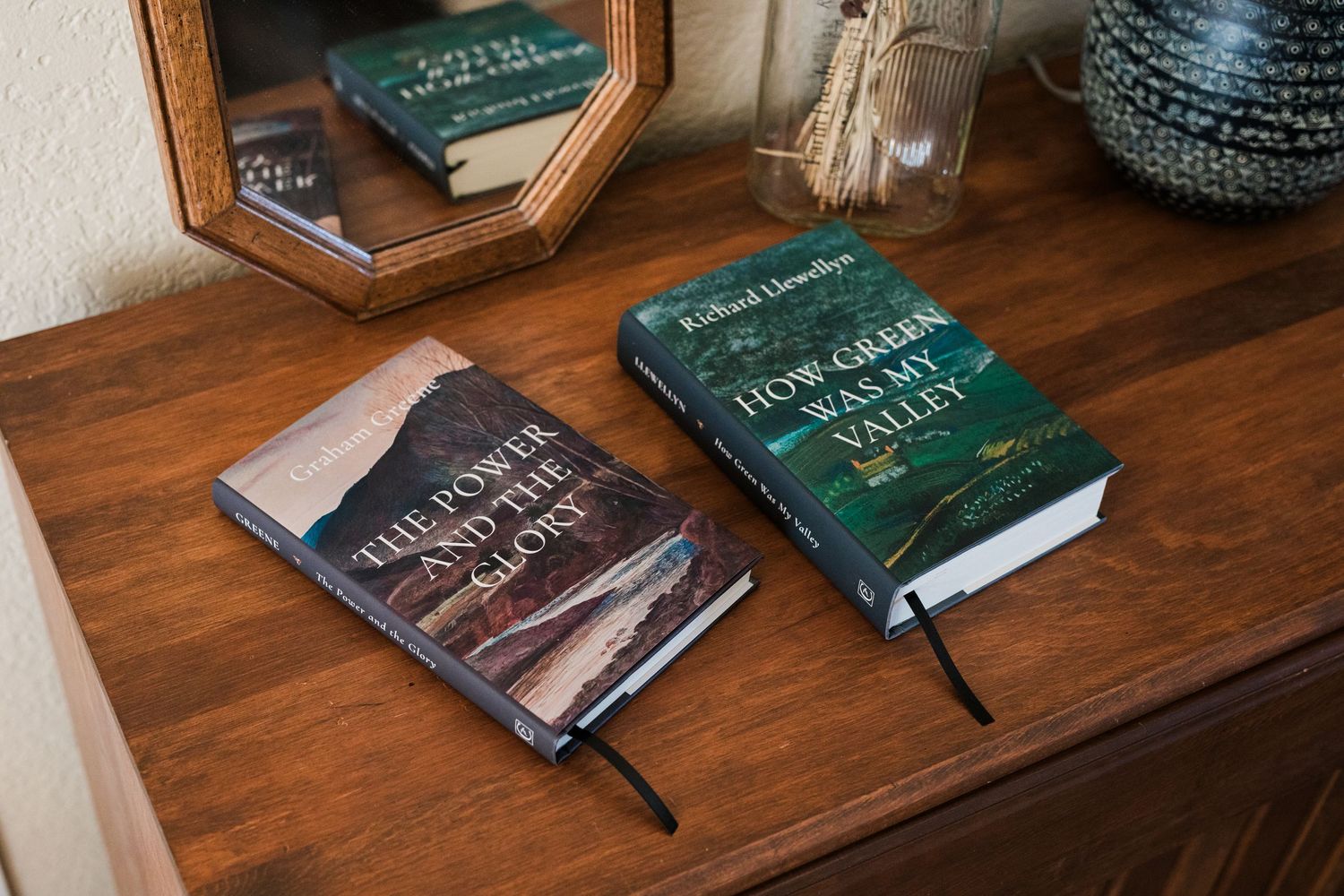 Two classic hardcover books on a wooden dresser near a mirror, including How Green Was My Valley by Richard Llewellyn.