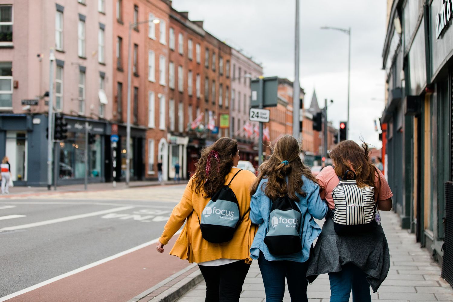 Four young women with backpacks walking along a colorful urban street in Ireland.